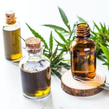 CBD oil in glass bottles and cannabis leaves at white table